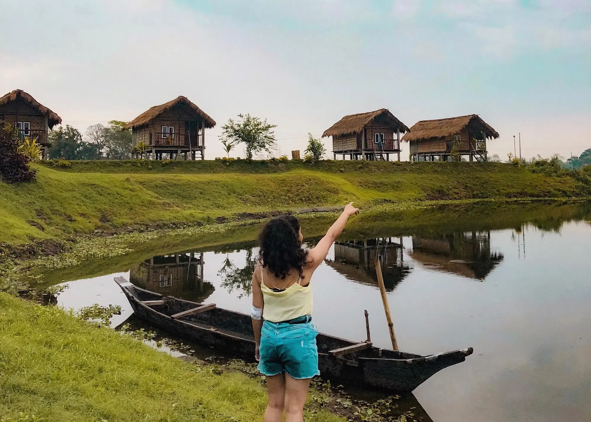 Majuli's lush green paddy fields stretch out under a vibrant blue sky, bordered by serene water bodies and dense vegetation.