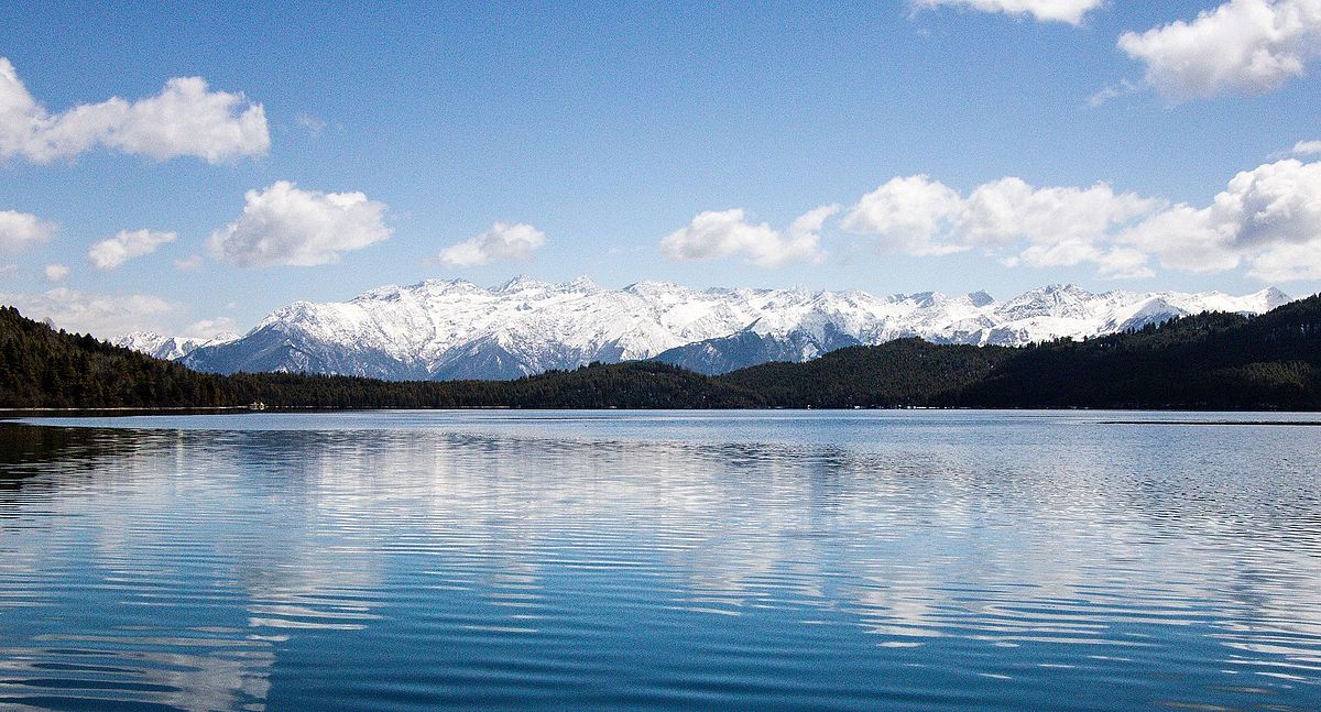 A panoramic shot of Rara Lake at sunrise, with the golden light illuminating the lake and the majestic Himalayas in the background. 