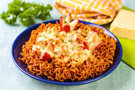 Semangkuk mie goreng keju dengan keju cheddar parut yang meleleh sempurna, dilengkapi topping daun bawang dan cabai iris